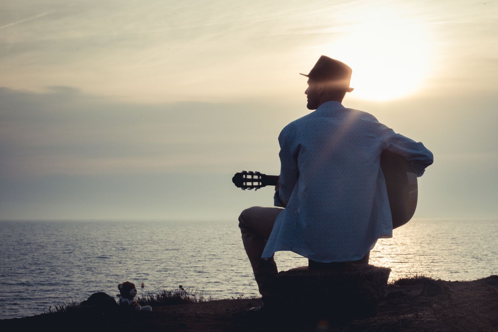 Cédric B. de dos, guitare à la main, face à la mer au coucher du soleil