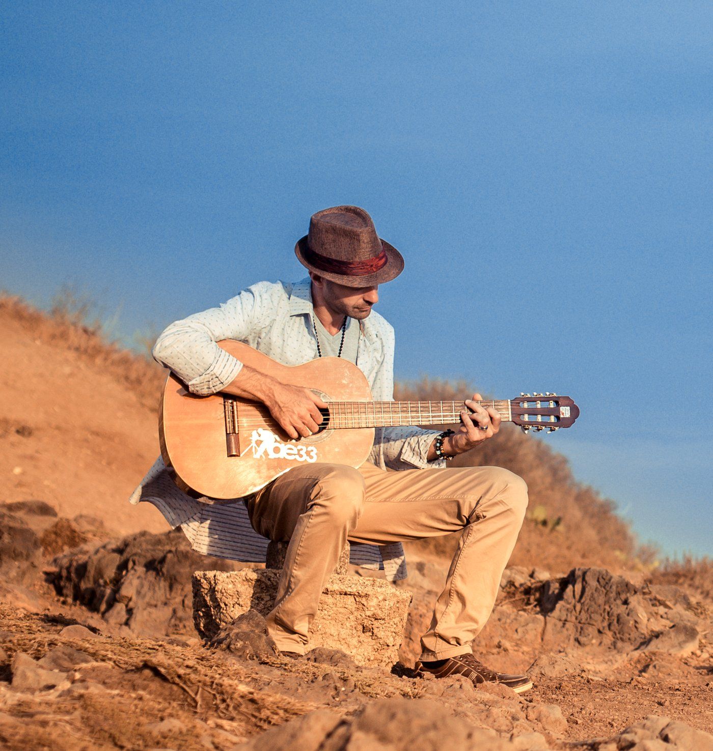Cédric B. à la guitare, assis sur les rochers, sous un ciel bleu